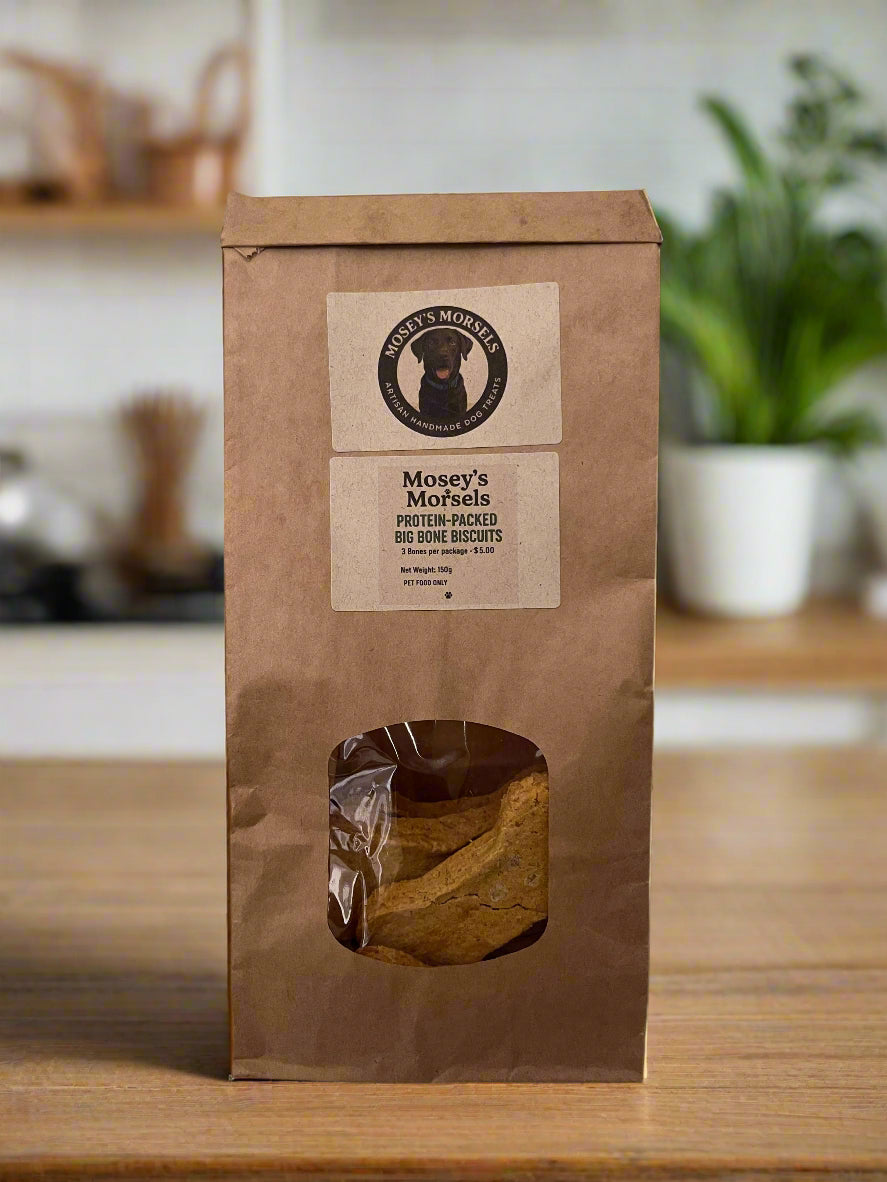 Brown paper bag with a window displaying a dog treat, branded 'Mosey's Morsels', on a white tiled wall background.