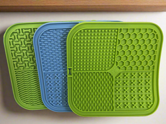 Three green and blue textured mats on a white surface with a tiled wall background.