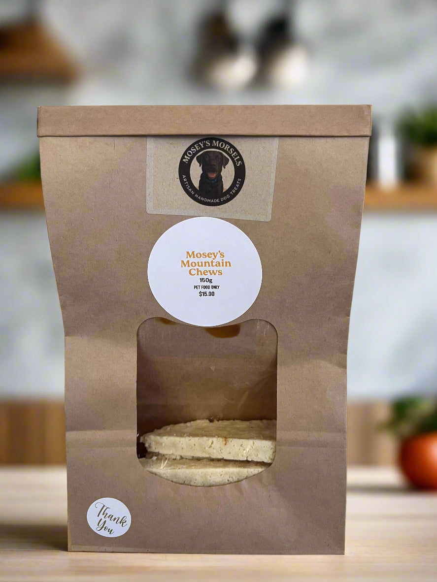 Kraft paper packaging with a window showing cookies, branded 'Mosey's Mountain Cheeks', on a tiled kitchen counter.